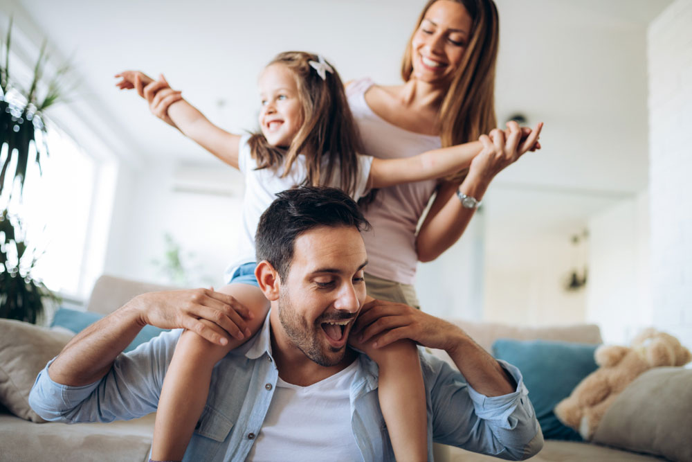happy young family with young daughter on father's shoulders, held by mother